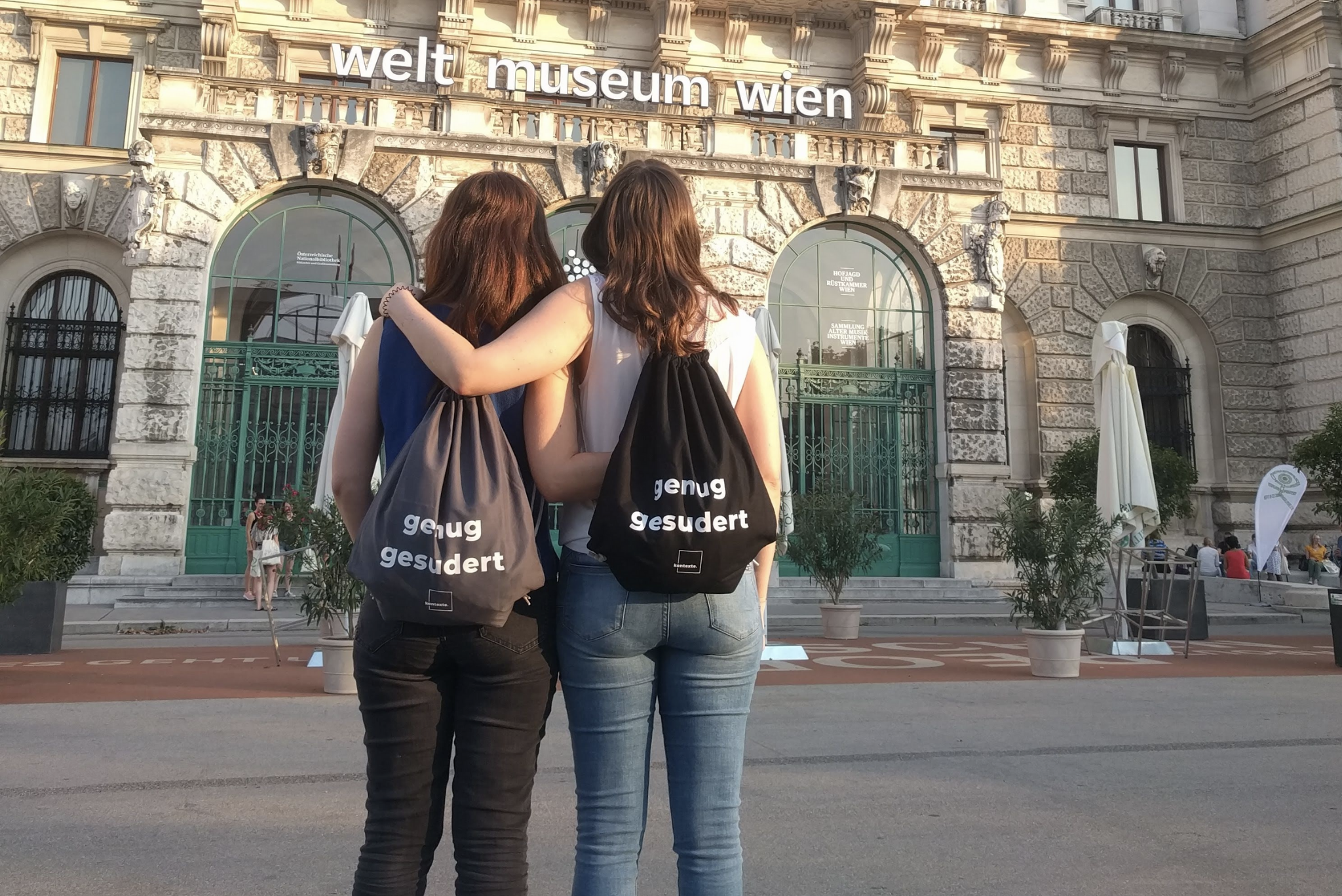 2 junge Frauen vom Verein kontexte präsentieren ihre City-Rucksäcke, Aufdruck: "genug gesudert"