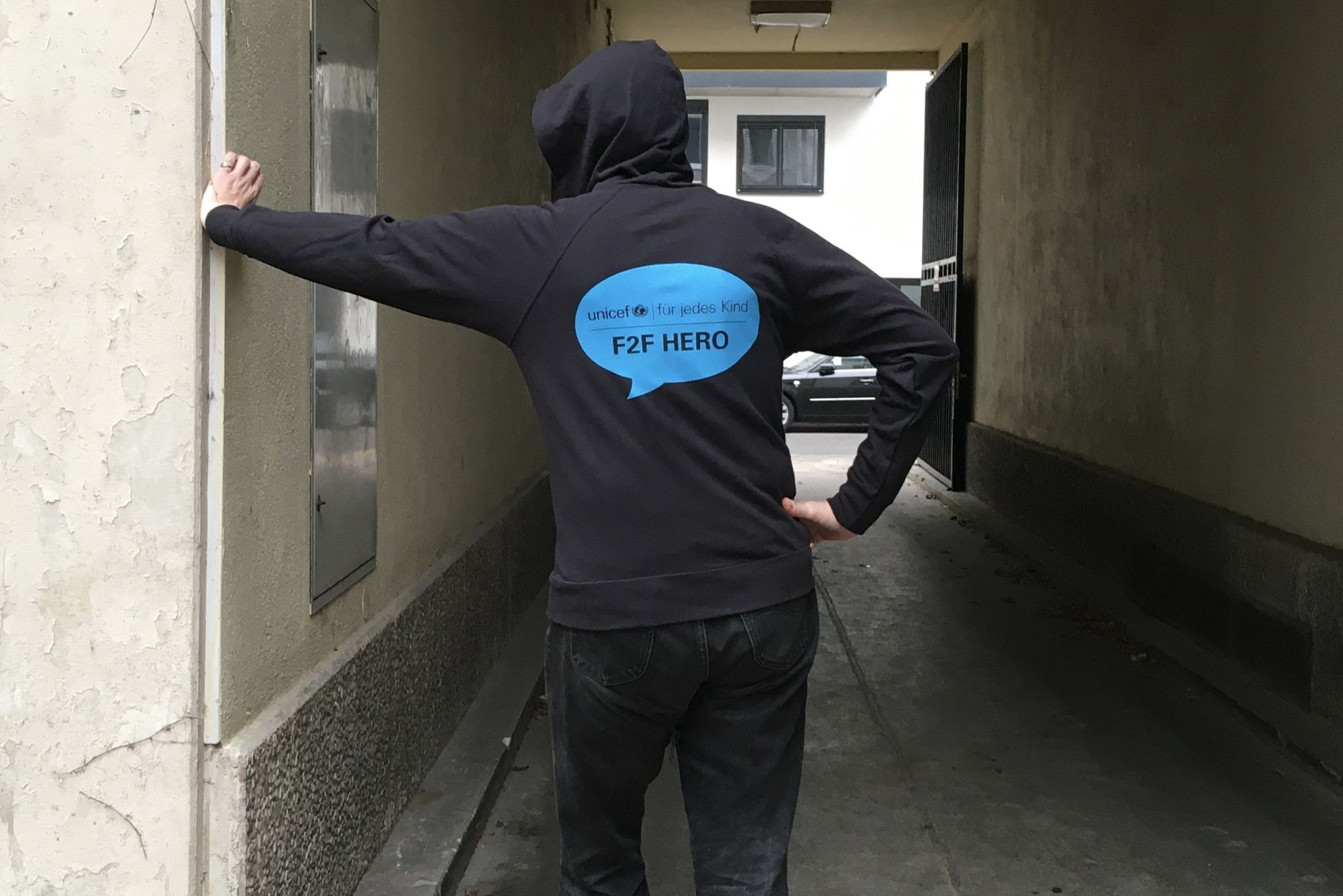 Junger Mann präsentiert frisch bedruckten UNICEF-Hoody mit dem Logo "F2F Hero" auf dem Rücken