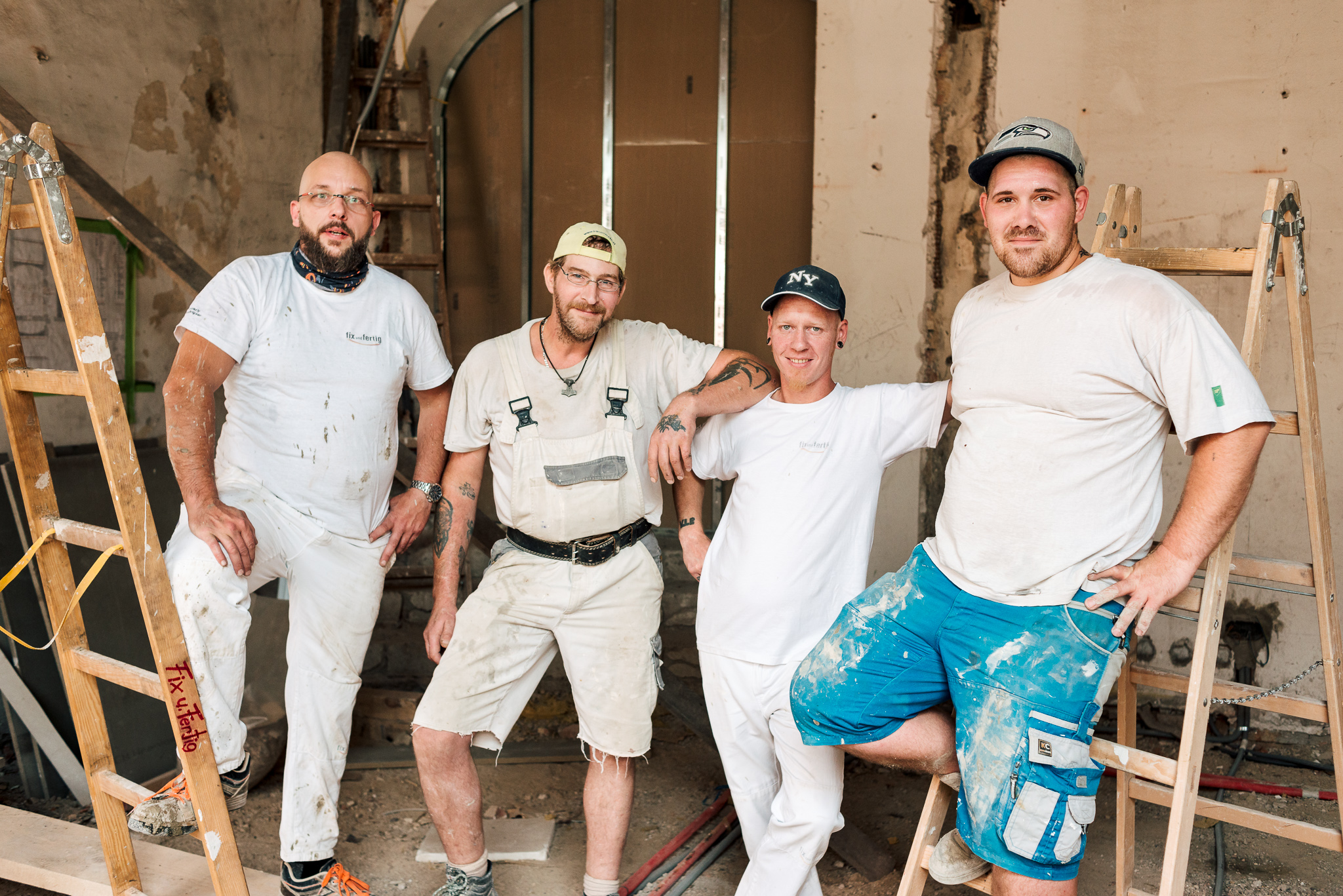 Gruppenbild auf der Baustelle: 4 Bauarbeiter lächeln erschöpft und entspannt in die Kamera